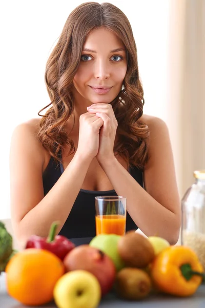 Chica sentada en la cocina en el escritorio con frutas y vasos con jugo —  Fotos de Stock