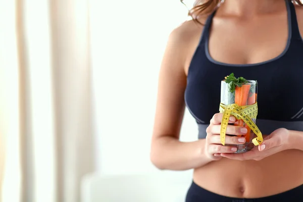 Mujer sosteniendo un vaso lleno de ensalada de frutas frescas con una cinta métrica alrededor del vaso —  Fotos de Stock