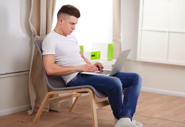 Dizüstü bilgisayar ile sandalye üzerinde oturan genç adam — Stok fotoğraf