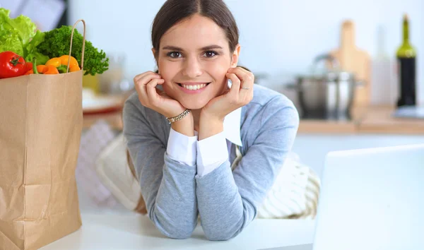 Portræt af en smilende kvinde madlavning i sit køkken sidder - Stock-foto