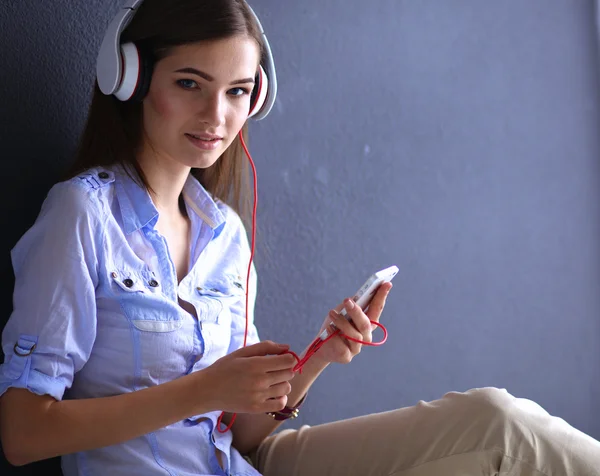 Smiling girl with headphones sitting on the floor near wall — Stock Photo, Image