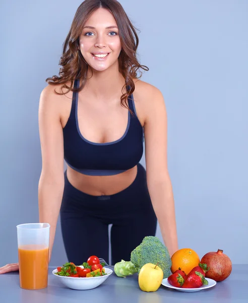 Mujer joven y hermosa de pie cerca del escritorio con verduras —  Fotos de Stock