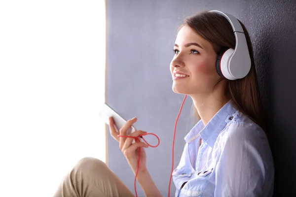 Menina sorridente com fones de ouvido sentado no chão perto da parede — Fotografia de Stock