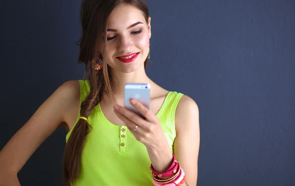 Mujer joven de pie cerca de la pared oscura con teléfono — Foto de Stock