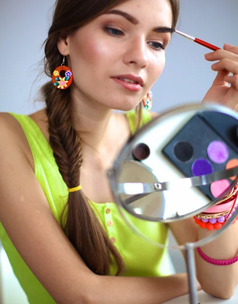 Unga vackra kvinnan att göra make-up nära spegeln, sitter vid skrivbordet — Stockfoto