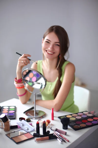 Jovem bela mulher fazendo maquiagem perto do espelho, sentado na mesa — Fotografia de Stock