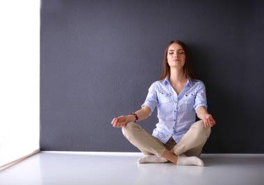 Genç bir kadın yerde, kara duvarın yanında oturuyor.