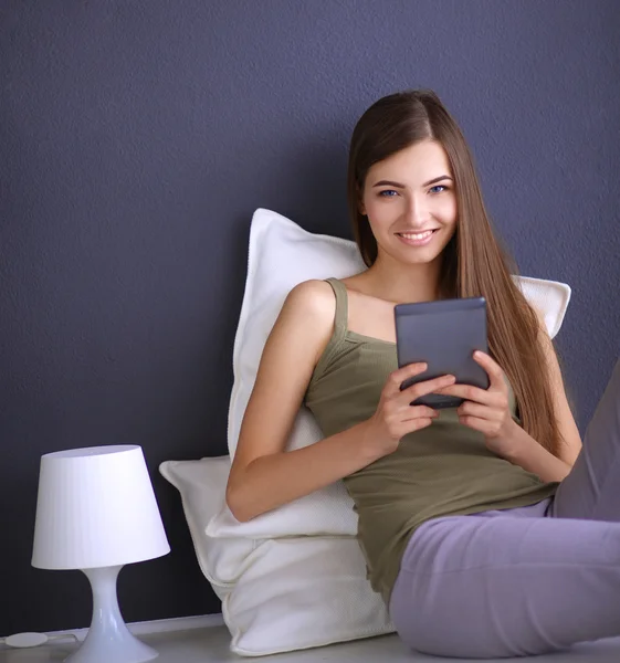 Mujer morena bonita sentada en el suelo con una almohada y mesa de avión — Foto de Stock