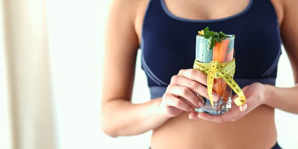 Mujer sosteniendo un vaso lleno de ensalada de frutas frescas con una cinta métrica alrededor del vaso —  Fotos de Stock