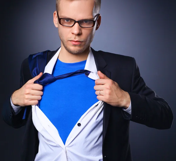 Joven hombre de negocios actuando como un súper héroe y rasgando su camisa, aislado sobre un fondo gris — Foto de Stock