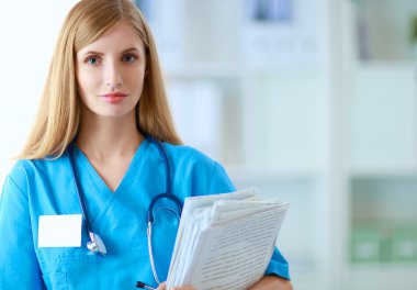 Hastane koridorunda klasörlü kadın doktor portresi.