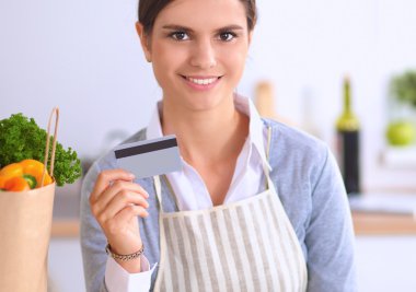 Mutfakta bilgisayar ve kredi kartı kullanan gülümseyen bir kadın.