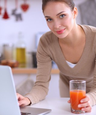 mutfağında suyu yudumlarken bir dizüstü bilgisayar kullanan kadın