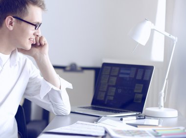 Genç işadamı ofiste çalışıyor, masada oturuyor.