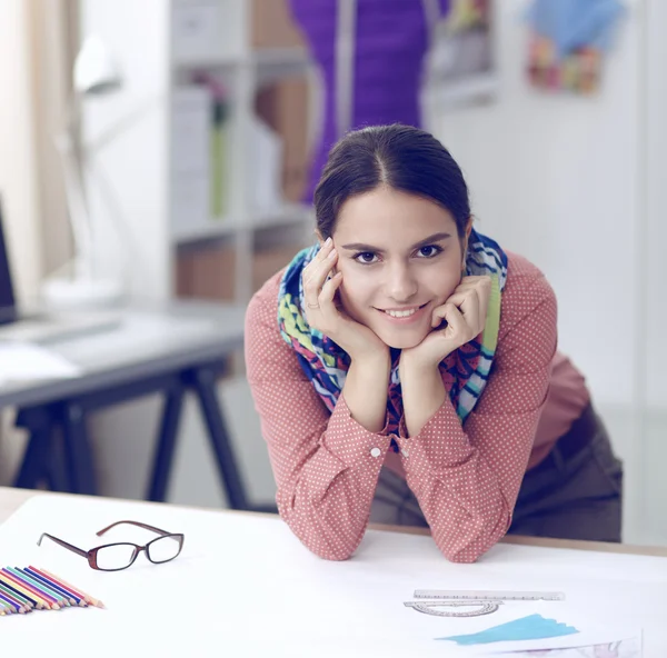 Joven y atractiva diseñadora de moda femenina trabajando en el escritorio de la oficina, dibujando mientras habla en el móvil — Foto de Stock