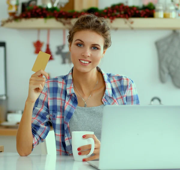 Mutfakta bilgisayar ve kredi kartı kullanan gülümseyen bir kadın. — Stok fotoğraf