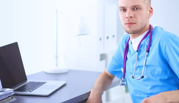 Ritratto di un medico maschio sorridente con computer portatile seduto alla scrivania nello studio medico — Foto Stock