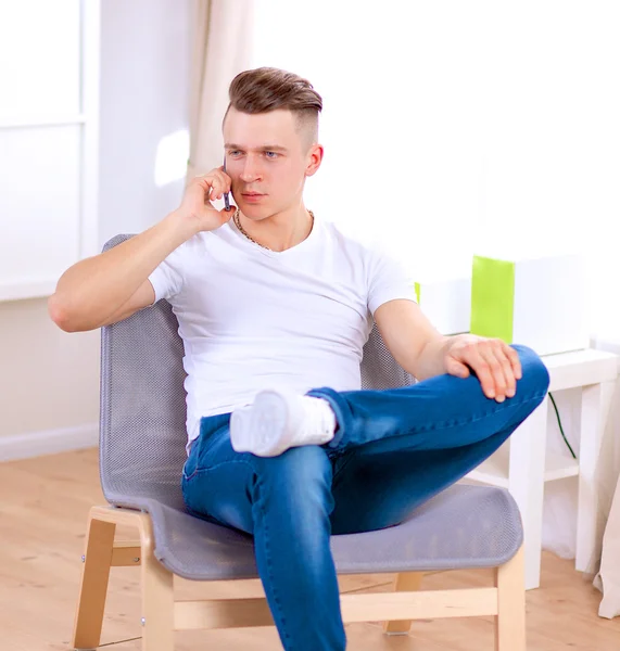 Mladý muž sedí na židli a mluví na mobilním telefonu — Stock fotografie