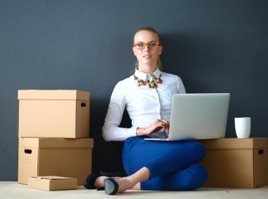 Kadın yerde dizüstü bilgisayarlı bir kutunun yanında oturuyor.