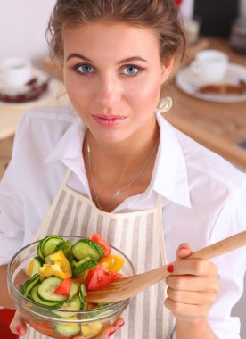 Genç kadın modern mutfakta taze salata yiyor.