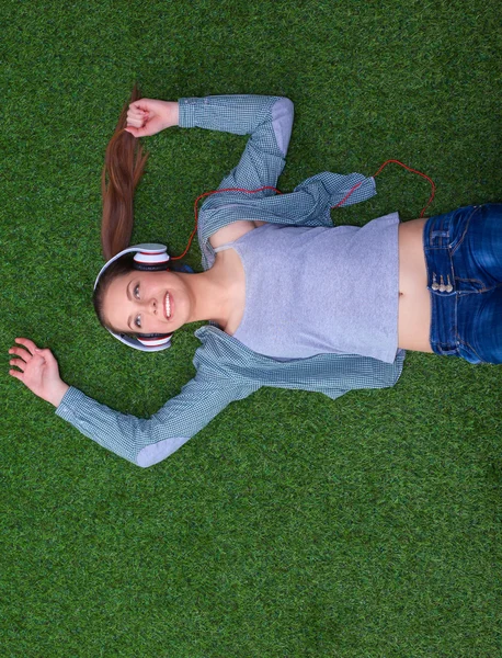 ヘッドフォンを草の上に寝そべって音楽を聞いているリラックスした女性 — ストック写真