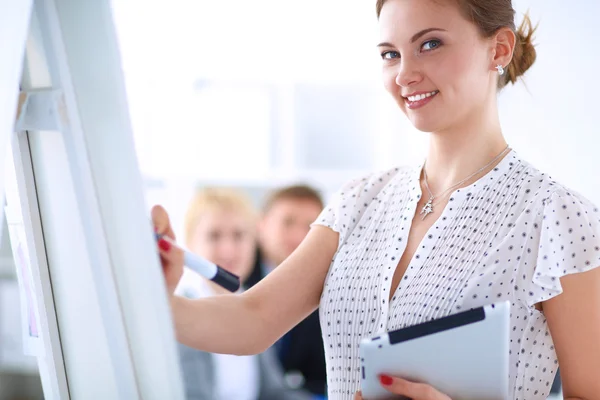 Businesswoman writing on flipchart while giving presentation to colleagues in office — Stock Photo, Image