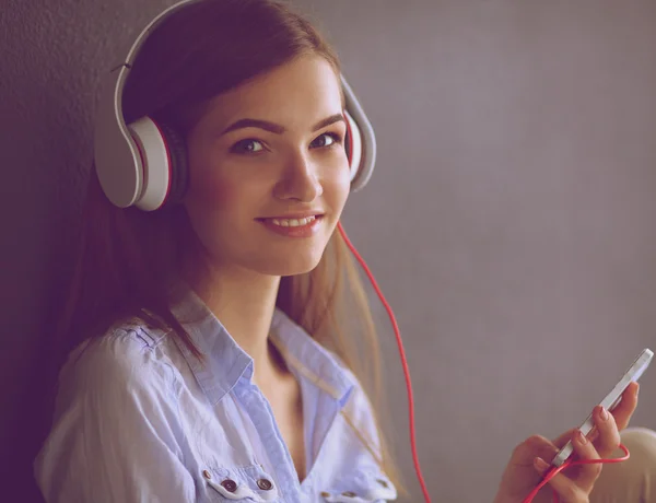 Usměvavá dívka s sluchátka sedí na podlaze u zdi — Stock fotografie
