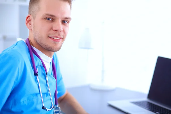 Ritratto di un medico maschio sorridente con computer portatile seduto alla scrivania nello studio medico — Foto Stock