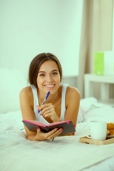 Young beautiful woman lying in bed writing a diary