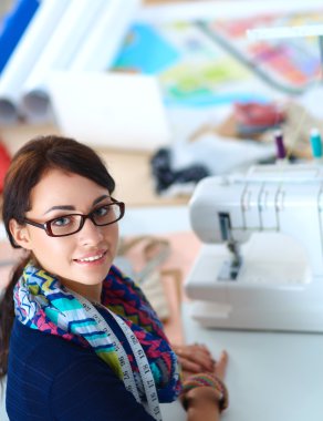 Güzel moda tasarımcısı stüdyoda masada oturuyor.