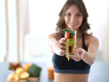 Elinde bir bardak dolusu taze meyve salatası ve bardağın etrafında mezura tutan bir kadın.