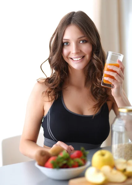 Chica sentada en la cocina en el escritorio con frutas y vasos con jugo —  Fotos de Stock