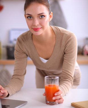 mutfağında suyu yudumlarken bir dizüstü bilgisayar kullanan kadın