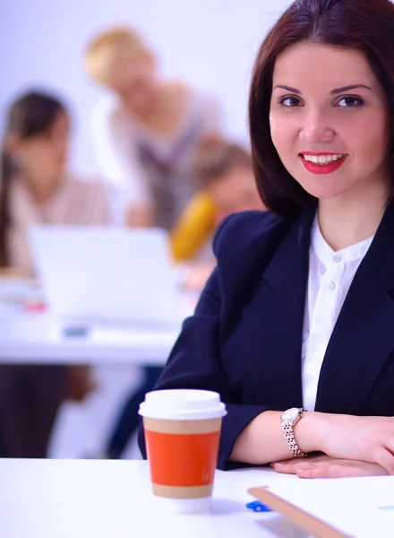 Atraktivní podnikatelka sedí na stole v kanceláři s šálkem kávy — Stock fotografie