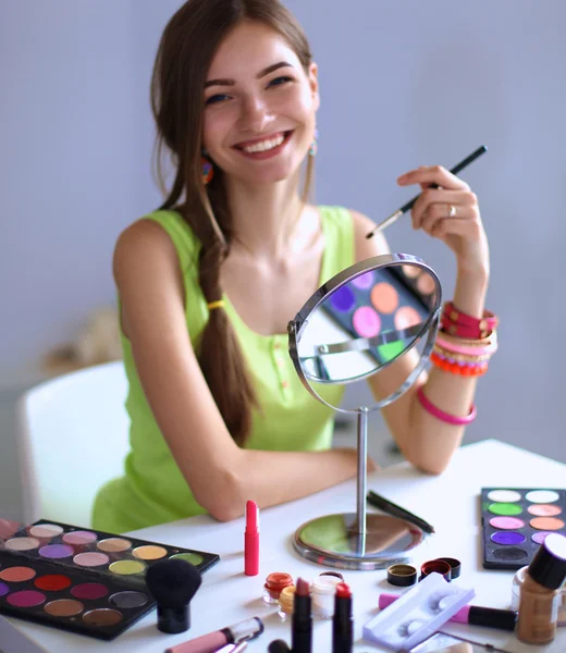 Joven hermosa mujer haciendo maquillaje cerca del espejo, sentado en el escritorio — Foto de Stock