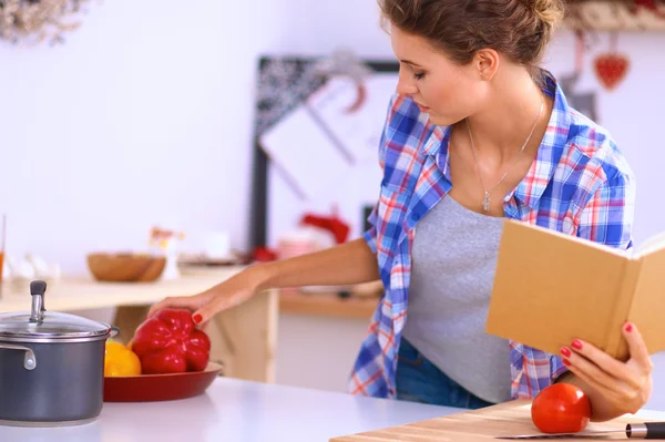 Mujer joven leyendo libro de cocina en la cocina, buscando receta — Foto de Stock