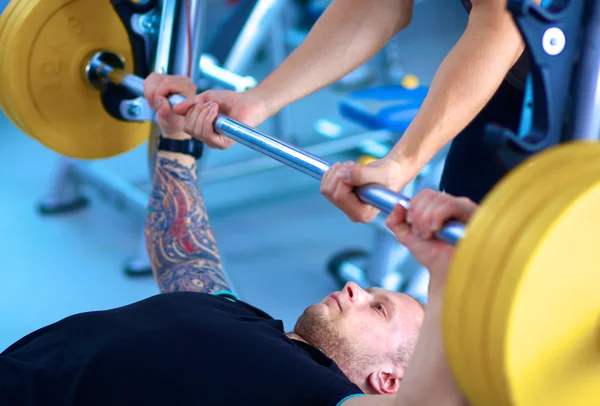 Jeune homme levant la barre dans la salle de gym avec instructeur — Photo