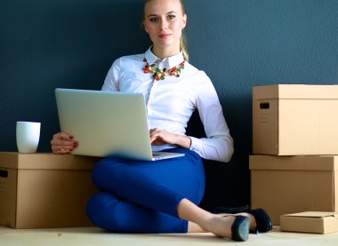 Kadın yerde dizüstü bilgisayarlı bir kutunun yanında oturuyor.