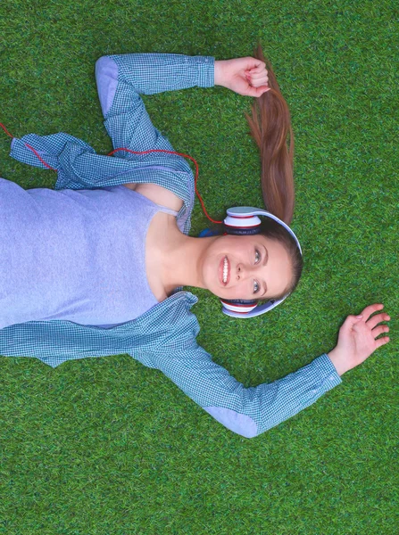 Relaxed woman listening to the music with headphones lying on  grass — Stock Photo, Image