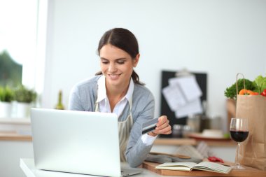 Mutfakta bilgisayar ve kredi kartı kullanan gülümseyen bir kadın.