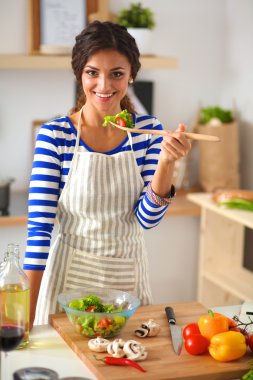 Genç kadın modern mutfakta taze salata yiyor.