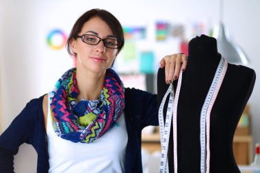 Gülümseyen moda tasarımcısı ofiste mankenin yanında duruyor.