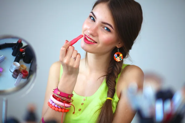 Молодая красивая женщина делает макияж возле зеркала, сидит за столом — стоковое фото