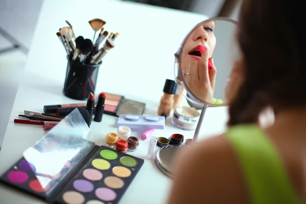 Joven hermosa mujer haciendo maquillaje cerca del espejo, sentado en el escritorio — Foto de Stock