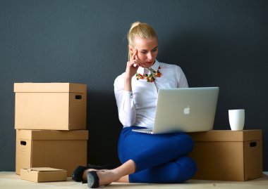Kadın yerde dizüstü bilgisayarlı bir kutunun yanında oturuyor.