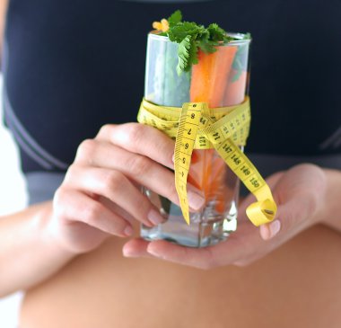 Elinde bir bardak dolusu taze meyve salatası ve bardağın etrafında mezura tutan bir kadın.