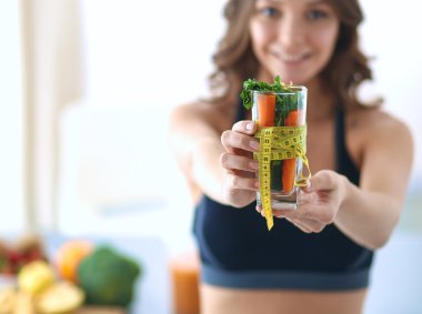 Elinde bir bardak dolusu taze meyve salatası ve bardağın etrafında mezura tutan bir kadın.