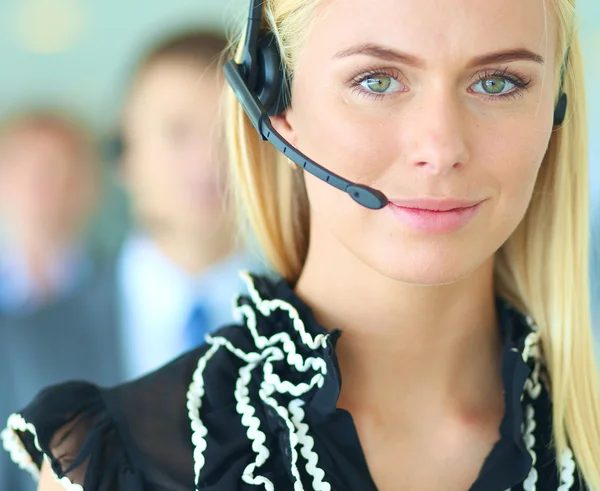 Mujer de negocios con auriculares sonriendo a la cámara en el centro de llamadas. Empresarios con auriculares en segundo plano —  Fotos de Stock