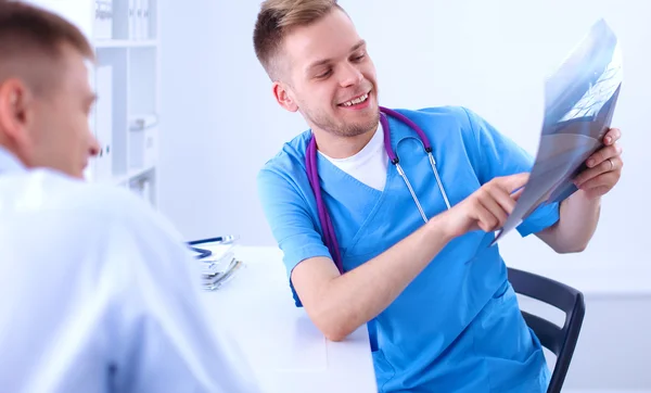 Retrato de um médico masculino sorridente com laptop sentado na mesa no consultório médico — Fotografia de Stock