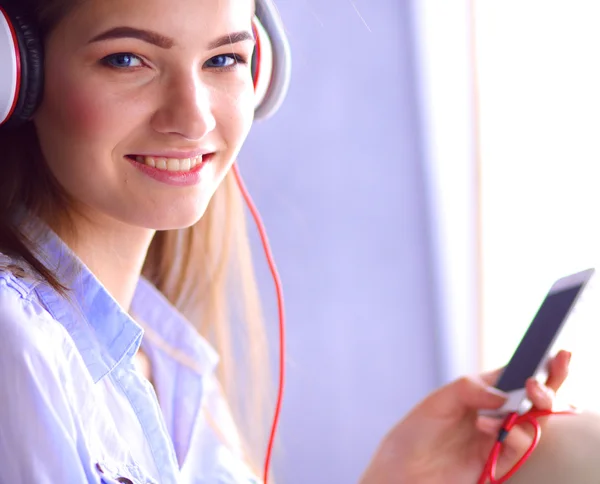 Ragazza sorridente con le cuffie seduto sul pavimento vicino al muro — Foto Stock